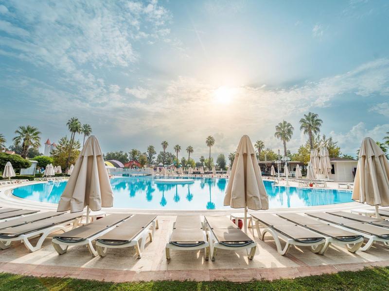 Sunset over a pool with lounge chairs and umbrellas in a tropical hotel garden.