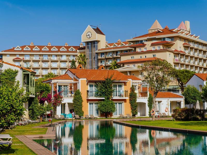 Large hotel building with multiple floors, red tiled roof, and pool in the foreground.
