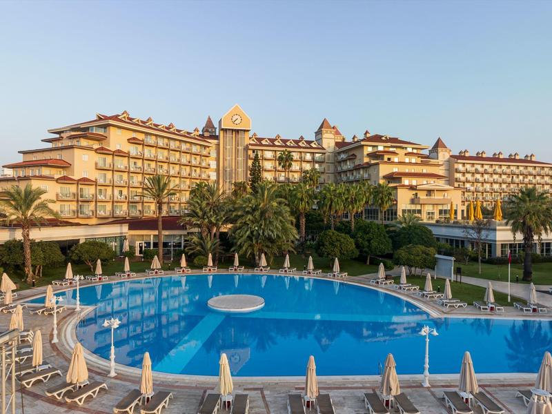 Large hotel complex with multiple floors, palm trees, and a round outdoor pool with loungers.