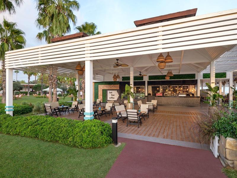 Open dining area with tables, chairs, and lamps in a tropical hotel setting.