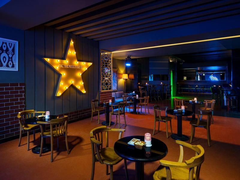 Cozy hotel bar area with illuminated star and several tables and chairs in a dark ambiance.
