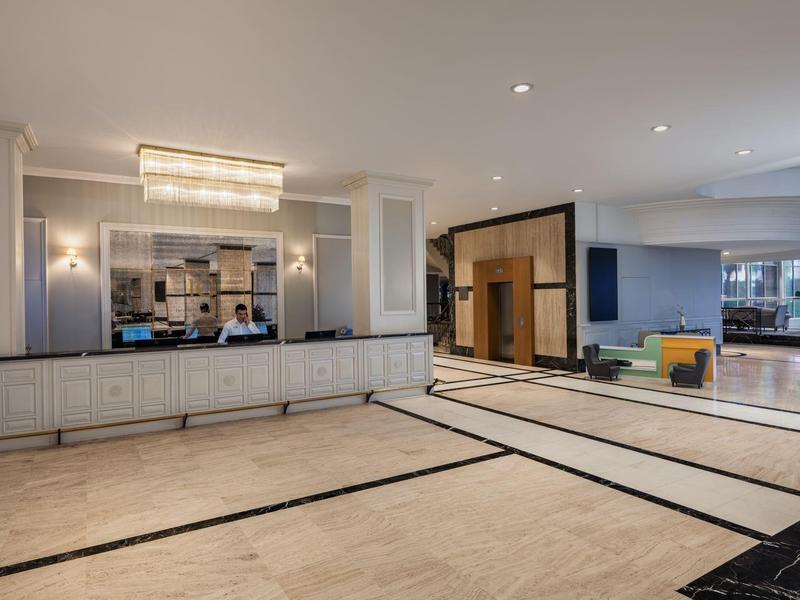 Spacious modern hotel lobby with light walls, large reception desk, and lounge area.