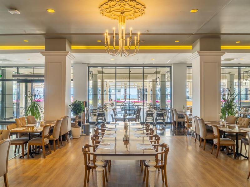 Bright, modern restaurant with wooden floors, elegant chandelier, and symmetrical table arrangement.