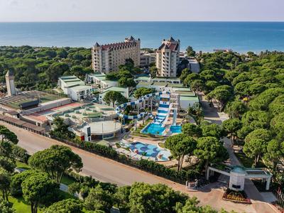 Large resort with pool, multiple buildings, and sea view surrounded by trees.