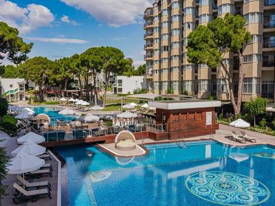 Large outdoor pool with sun loungers and trees next to a multi-story hotel.