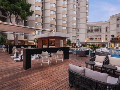 Modern hotel outdoor area with wooden deck, furniture, and tall buildings in the background