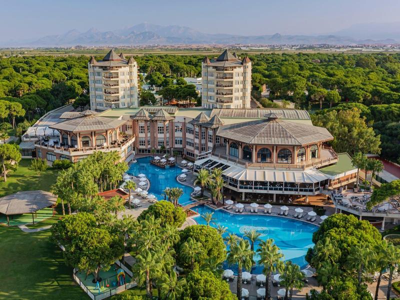 Luxury hotel with multiple buildings, large pool, and lush green surroundings under clear sky.