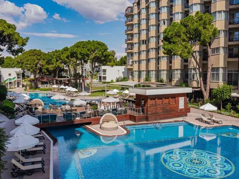 Large outdoor pool with sun loungers and trees next to a multi-story hotel.