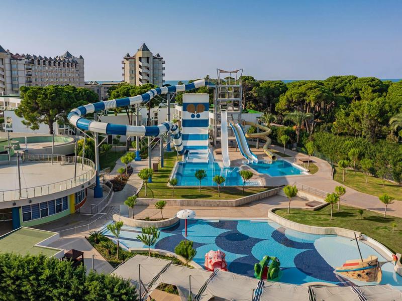 Water park with large water slides and swimming pools in front of hotel buildings amid greenery.