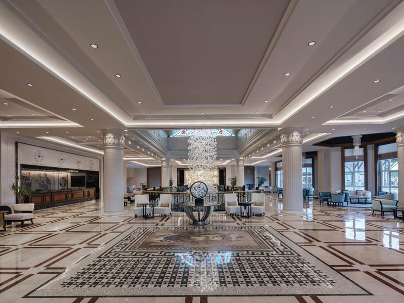 Spacious hotel lobby with seating areas, white columns, and elegant marble tile flooring.