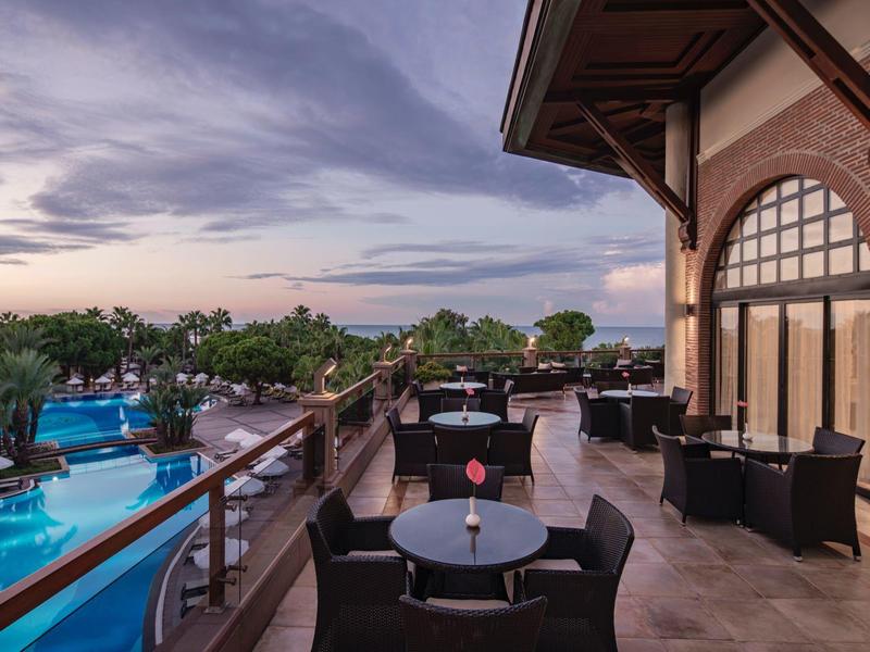 Balcony terrace with seating area overlooking an illuminated pool at sunset.