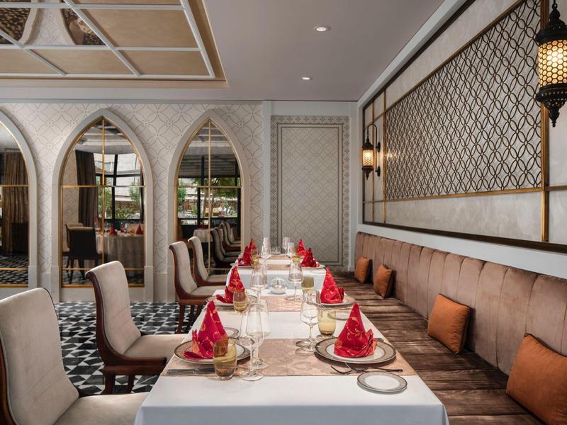 Elegant restaurant with white-set tables, red napkins, wall lamps, and cushioned benches.