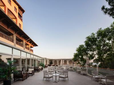 Terrazza esterna di un hotel con tavoli, sedie e alberi sotto un cielo limpido.