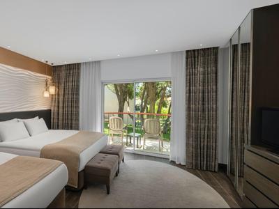 Modernes Hotelzimmer mit zwei Betten, hellem Holz, großem Fenster und Blick auf Garten.