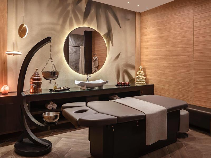 Modern wellness room with massage table, round mirror, and stylish decorations.