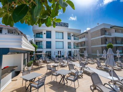 Espace piscine d'hôtel moderne avec chaises longues, tables et parasols sous un ciel bleu.