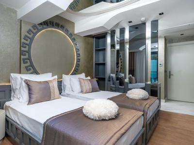 Habitación de hotel moderna con cama doble, espejo redondo grande y ducha de vidrio al fondo.