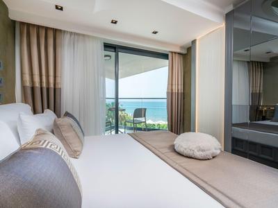 Chambre d'hôtel moderne avec grande fenêtre, vue sur la mer et balcon avec chaises.