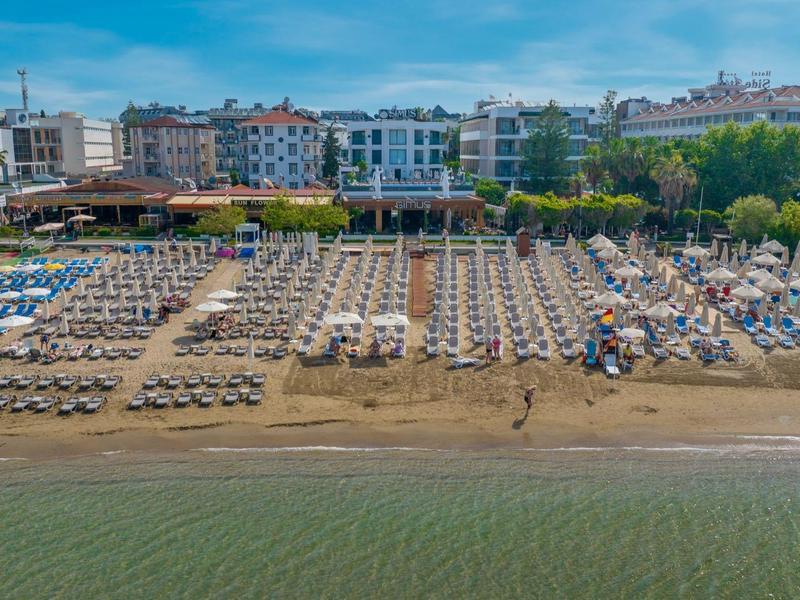 Playa llena de sombrillas y tumbonas frente a un edificio junto al agua en la ciudad.