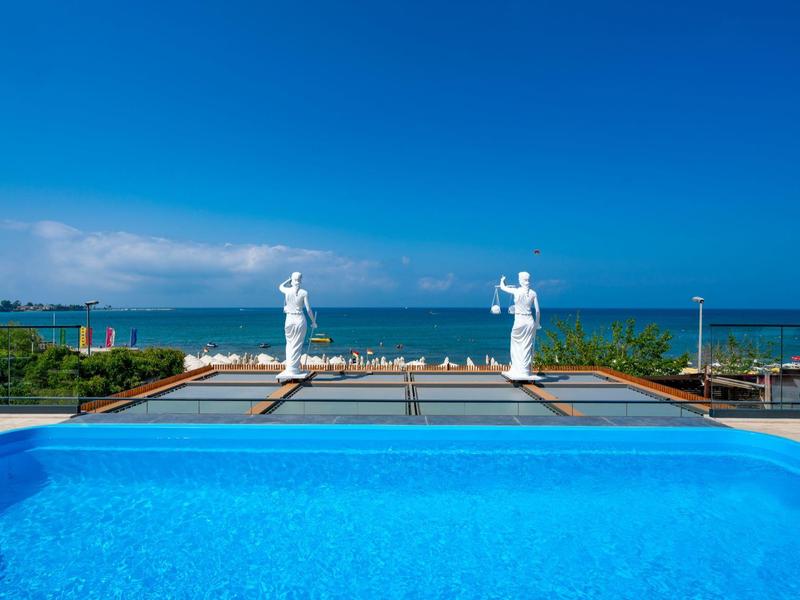 Vista de una piscina con dos estatuas blancas y el mar al fondo bajo cielo despejado.