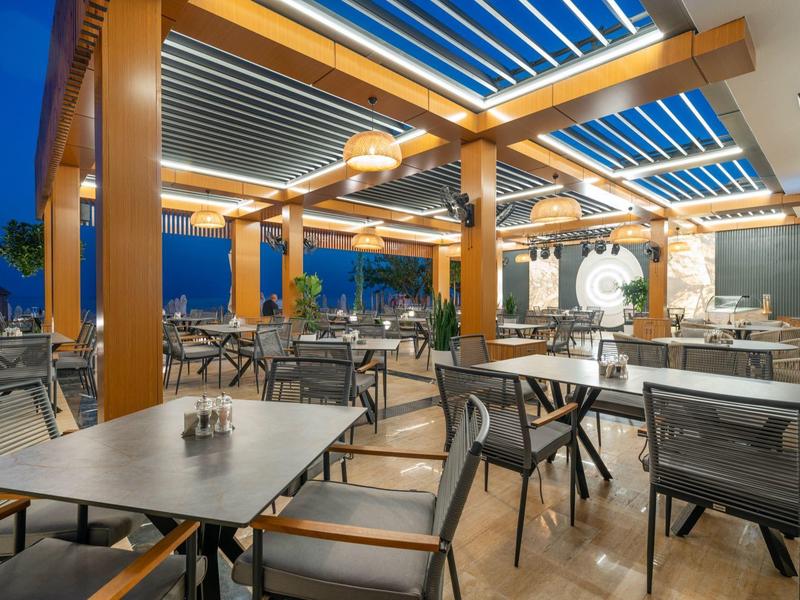 Terraza moderna al aire libre con mesas y sillas bajo un techo de pérgola de madera al atardecer.