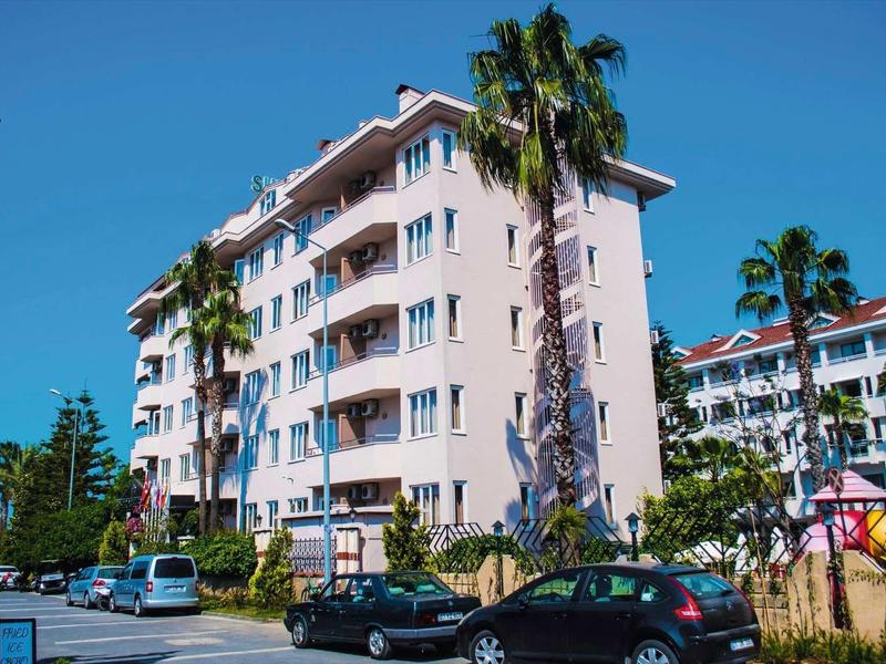 Mehrstöckiges rosa Gebäude mit Balkonen, Palmen und parkenden Autos unter blauem Himmel.