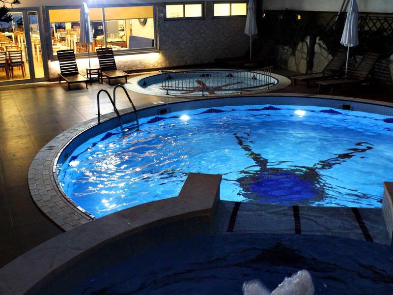 Drei beleuchtete runde Pools in der Nacht mit umliegenden Stühlen und Gebäuden.