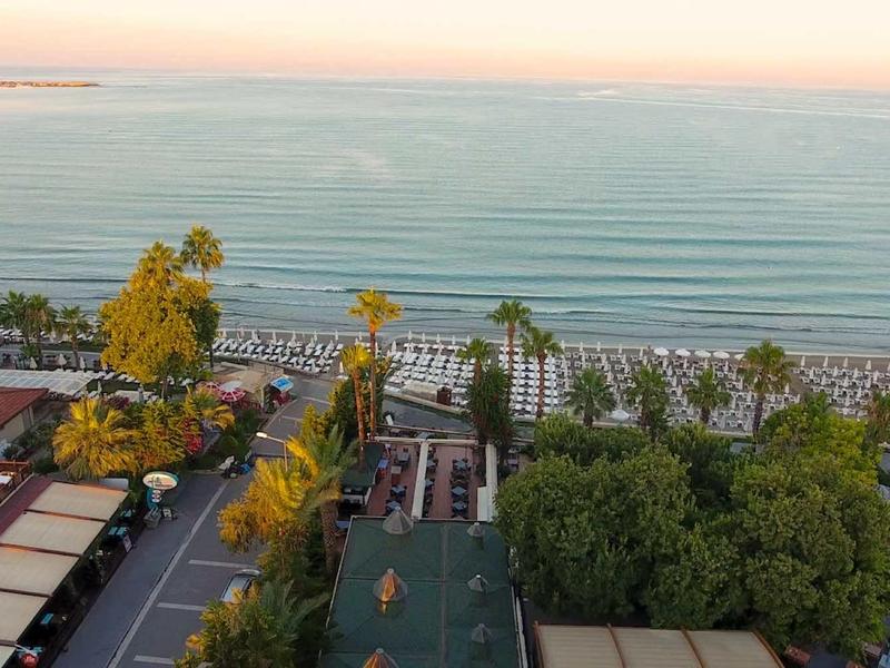 Küste mit ruhigem Meer, Palmen und Gebäuden an der Uferpromenade bei Sonnenuntergang.