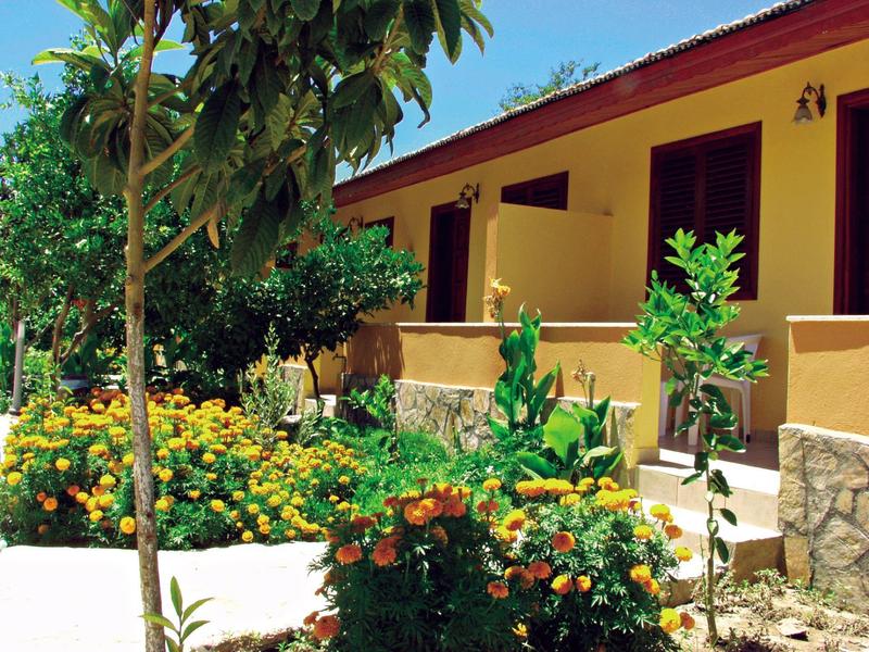 A holiday house with yellow walls and a flower garden in front under a blue sky.