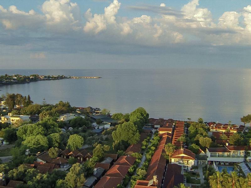 View of a coastal town with buildings, trees, and calm sea under a cloudy sky.