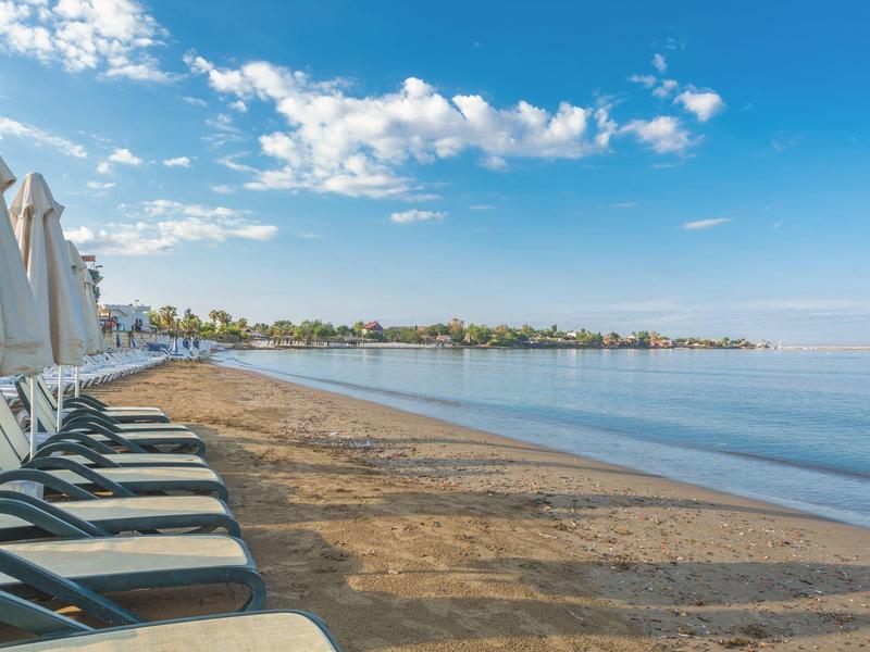Empty lounge chairs and closed umbrellas on a sandy beach under a blue sky with few clouds.
