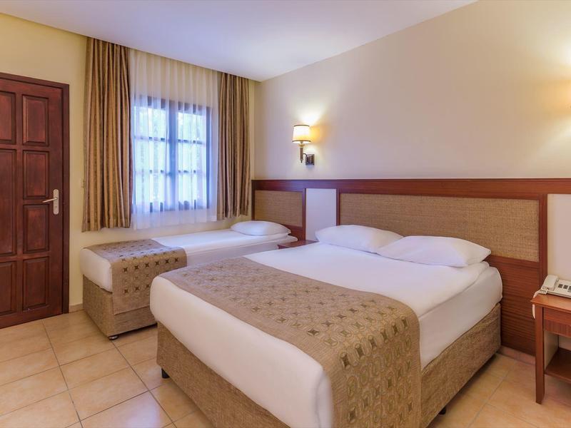 Hotel room with two beds, wooden door, curtains, and nightstands with lighting.