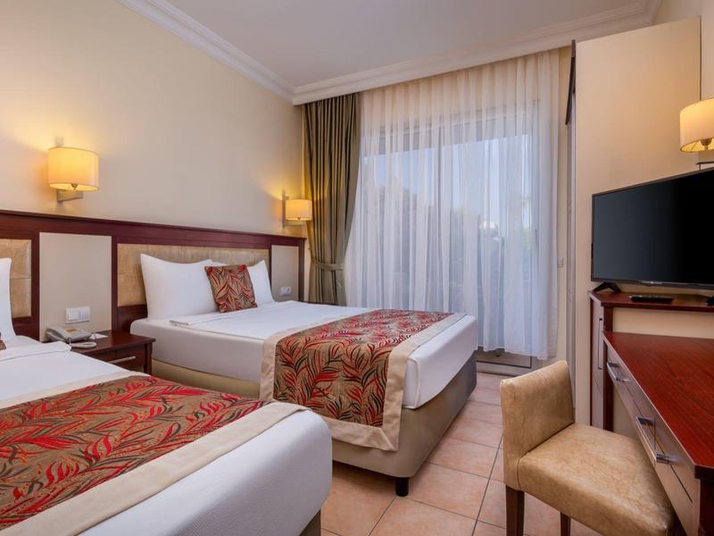 Hotel room with two single beds, desk, TV, and window with curtains.