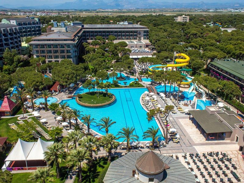 Hotel resort with large pool, water slides, palm trees, and lounge chairs under blue sky.