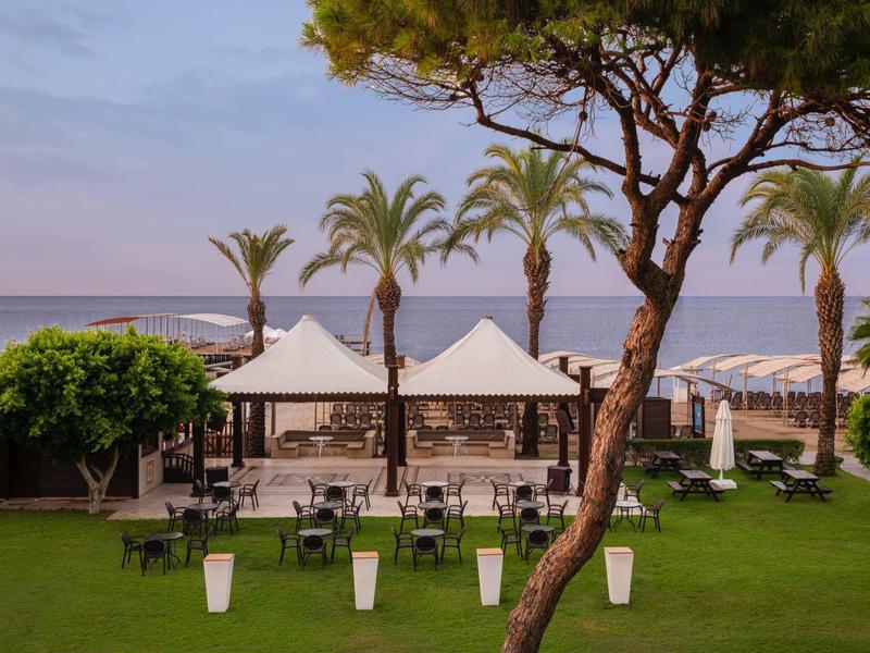Green garden with chairs under white tents by the sea at sunset
