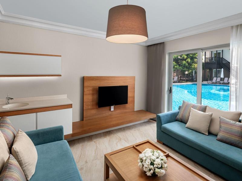 Modern living room with two sofas, wall-mounted TV, wooden table, and a view of the pool.