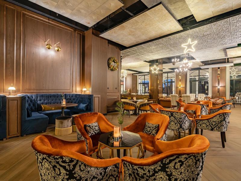 Elegant hotel restaurant with cozy orange armchairs and blue upholstered sofa, decoratively lit.