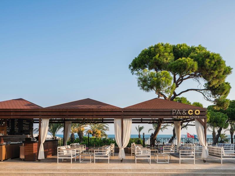 Open beach restaurant with white furniture and sea view under clear blue sky.