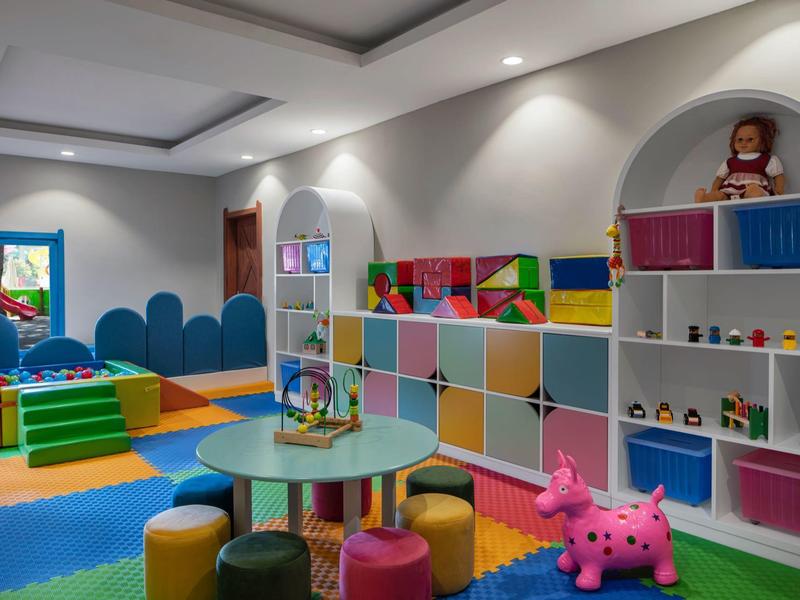 Colorful children's playroom with soft mats, stools, and shelves filled with toys.