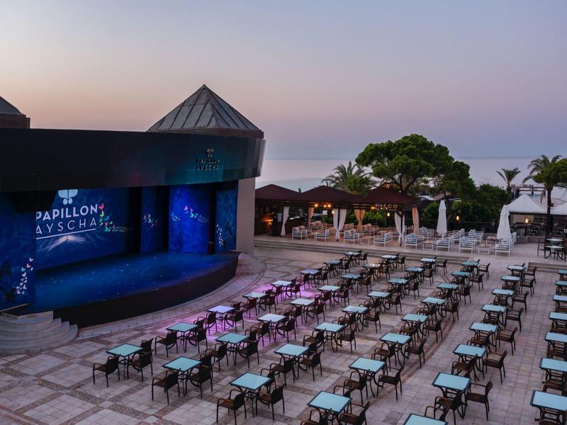 Evening view of an outdoor stage area with rows of chairs and a pool at a hotel resort.