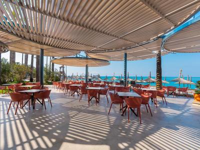 Open hotel terrace area with red chairs and sea view under sunny weather.