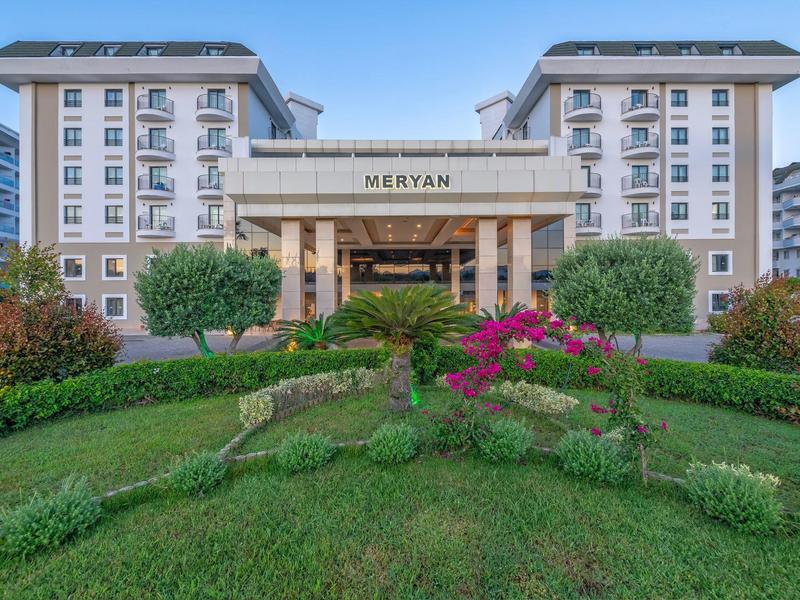 Complesso alberghiero moderno su più piani con giardino curato e cielo azzurro.
