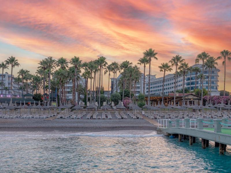 Tramonto sulla spiaggia, palme e hotel vicino all'acqua con un molo.