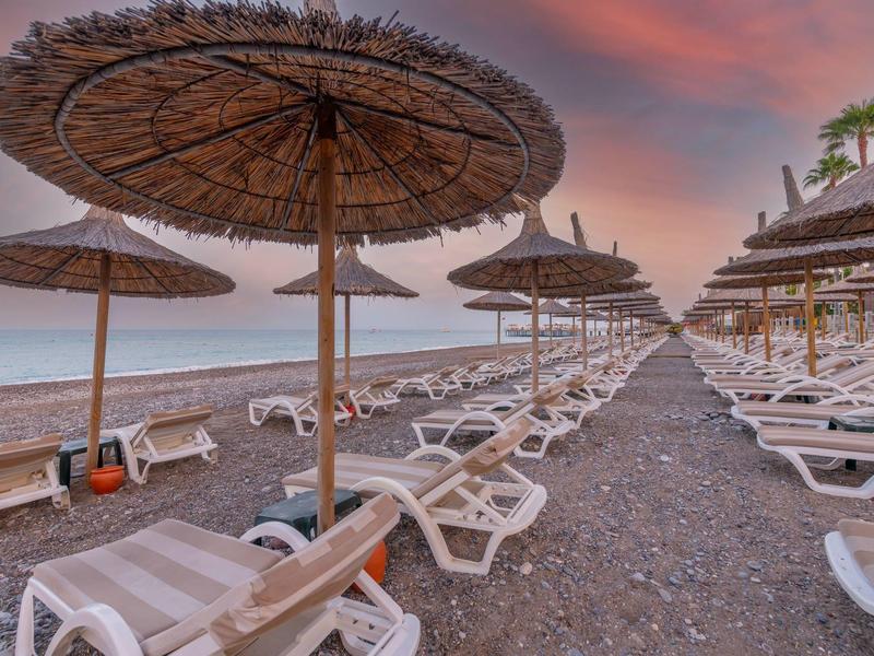 Spiaggia vuota con lettini e ombrelloni di paglia al tramonto vicino al mare.