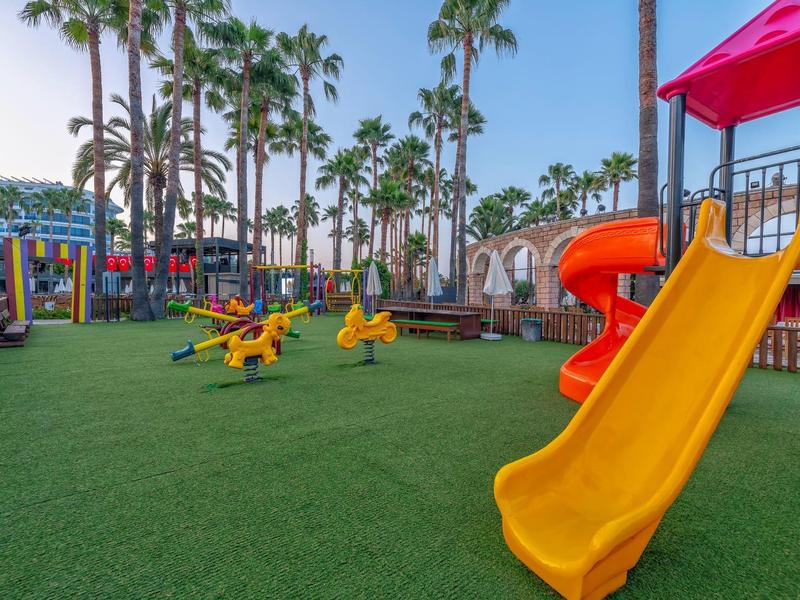 Parco giochi colorato per bambini con scivoli e giostre circondato da palme e edifici dell'hotel.