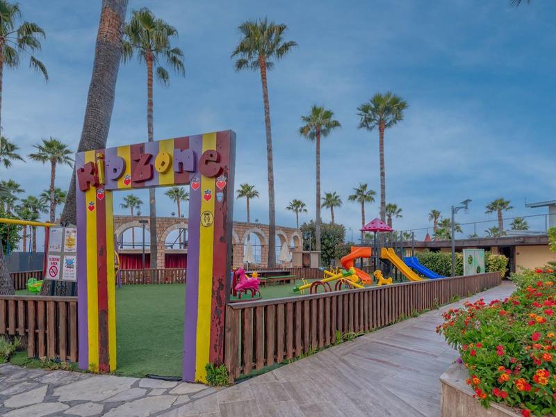 Area giochi per bambini con scivoli colorati e palme sotto un cielo limpido.