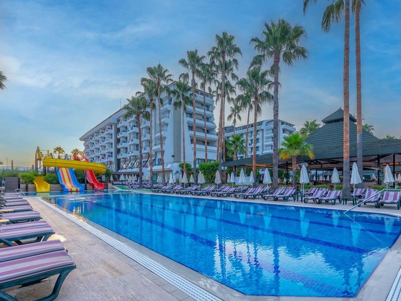Piscina moderna dell'hotel con cascate, scivoli e lettini sotto un cielo azzurro.