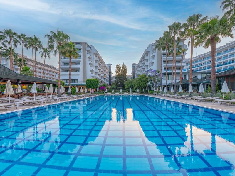 Grande piscina all'aperto con piastrelle blu, sedie a sdraio intorno e moderni edifici dell'hotel.