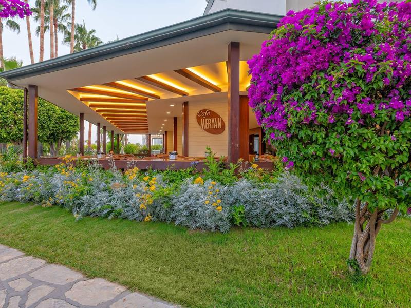 Hotel moderno con ampio portico, piante rigogliose e un albero con fiori viola vivaci