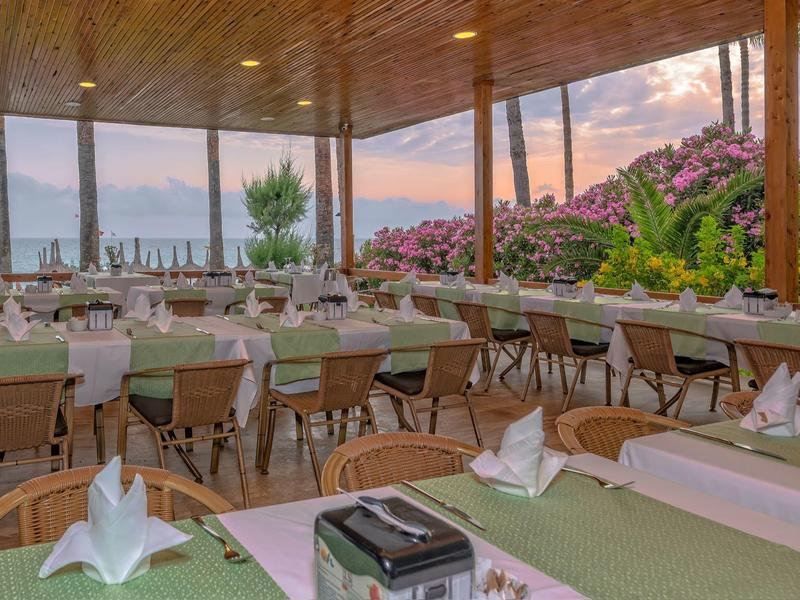Ristorante elegante con tavoli apparecchiati e vista su giardino e acqua al tramonto.